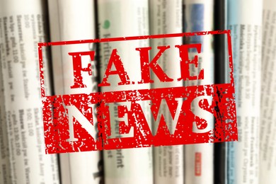 Image of Red Fake News stamp and newspapers as background, closeup