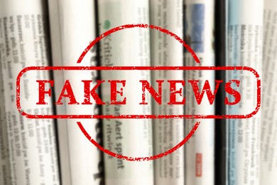 Image of Red Fake News stamp and newspapers as background, closeup