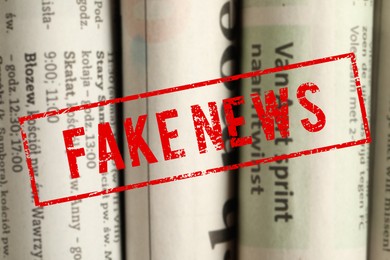 Image of Red Fake News stamp and newspapers in different languages as background, closeup