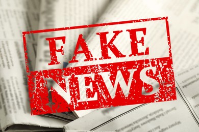 Image of Red Fake News stamp and newspapers as background, closeup