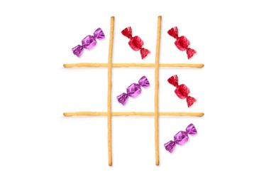 Image of Tic-tac-toe game made of different candies and grissini sticks on white background, top view