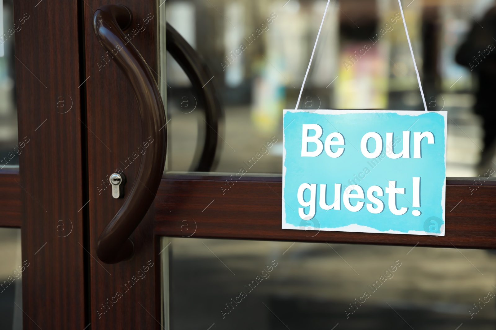 Image of Be Our Guest sign hanging on glass door outdoors
