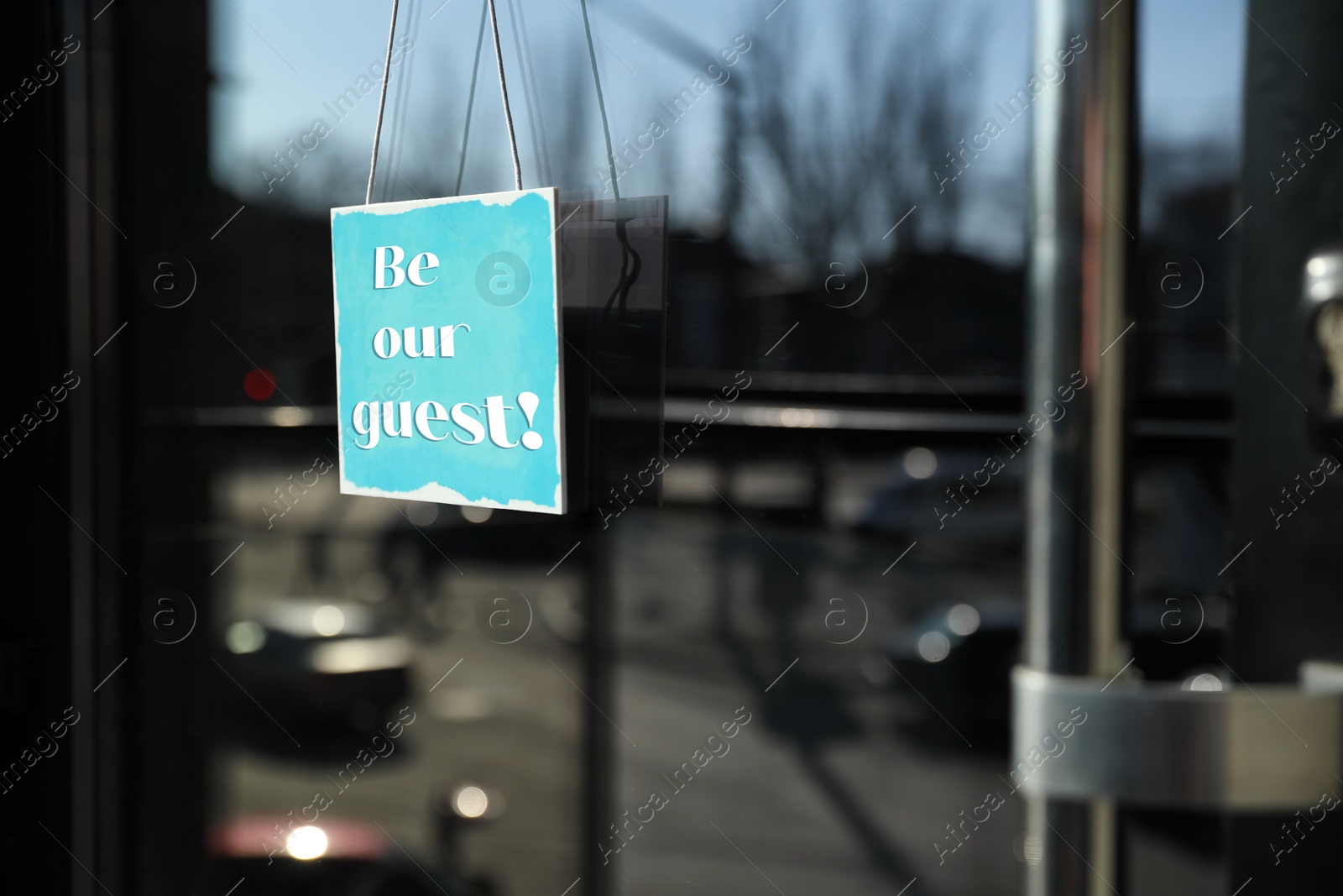 Image of Be Our Guest sign hanging on glass door outdoors
