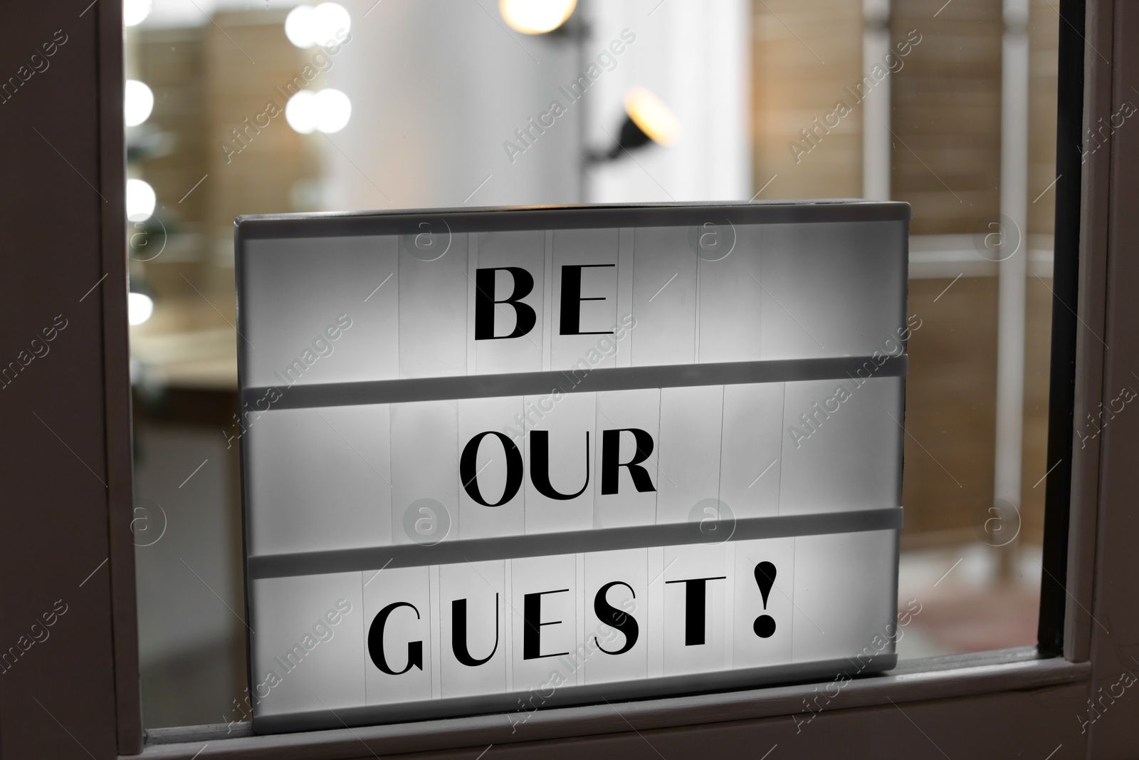 Lightbox with phrase Be Our Guest on glass door indoors Image of Lightbox with phrase Be Our Guest on glass door indoors