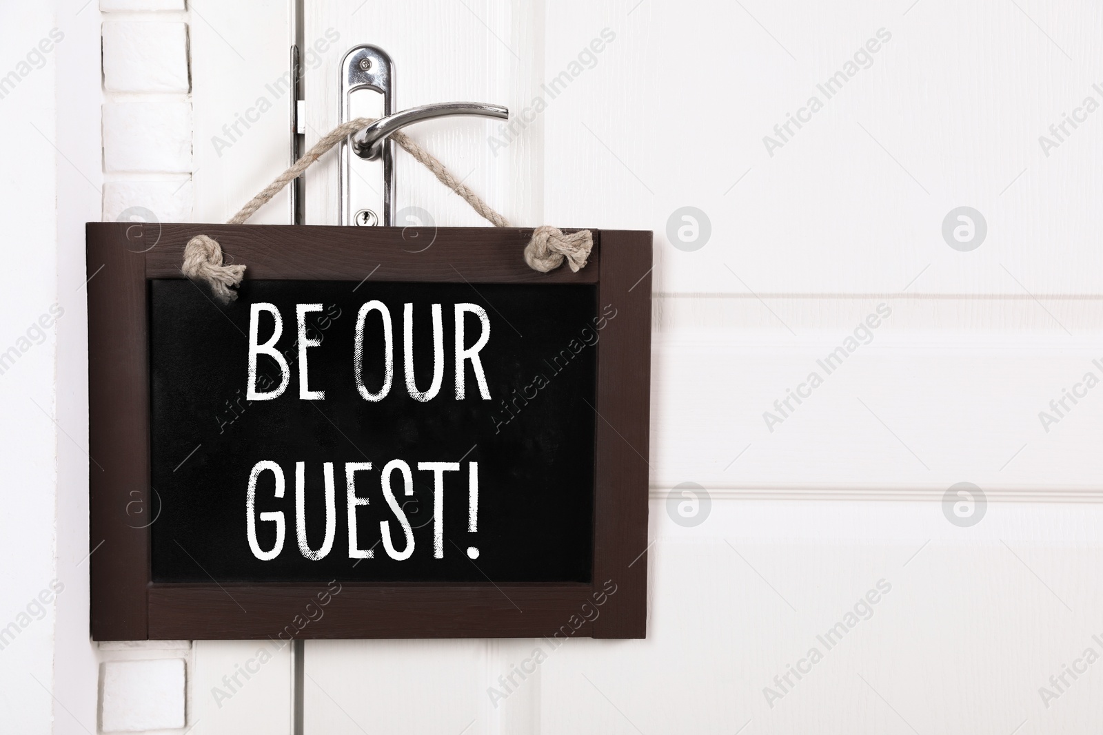 Small blackboard with phrase Be Our Guest hanging on door handle, space for text Image of Small blackboard with phrase Be Our Guest hanging on door handle, space for text