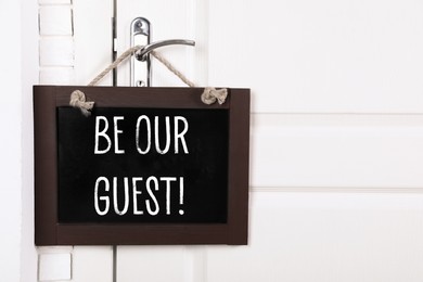 Image of Small blackboard with phrase Be Our Guest hanging on door handle, space for text
