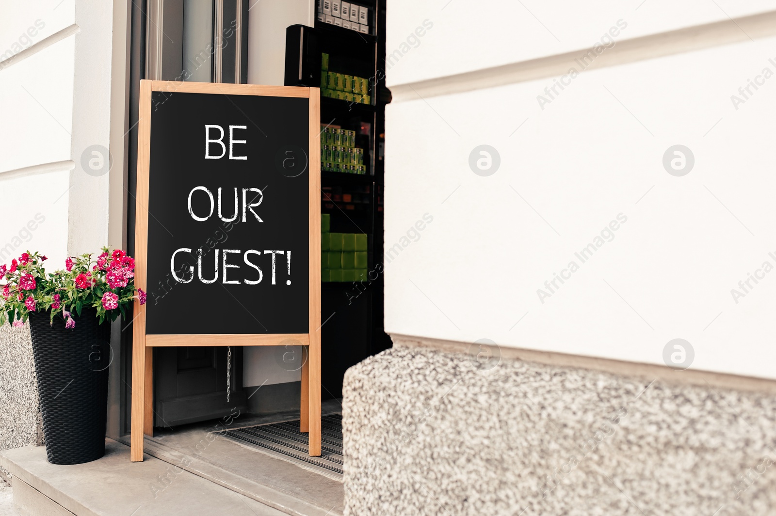 Image of Advertising board with phrase Be Our Guest and flower pot near cafe entrance