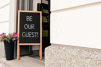 Image of Advertising board with phrase Be Our Guest and flower pot near cafe entrance