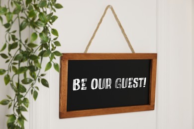 Image of Small blackboard with phrase Be Our Guest and houseplant hanging on white wall