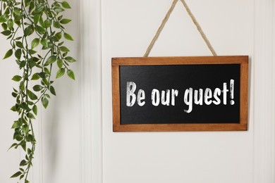 Image of Small blackboard with phrase Be Our Guest and houseplant hanging on white wall