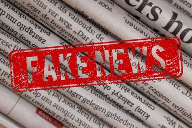 Image of Red Fake News stamp and newspapers in different languages as background, closeup