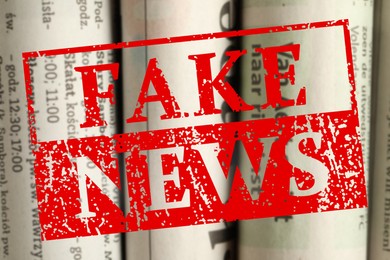 Image of Red Fake News stamp and newspapers in different languages as background, closeup