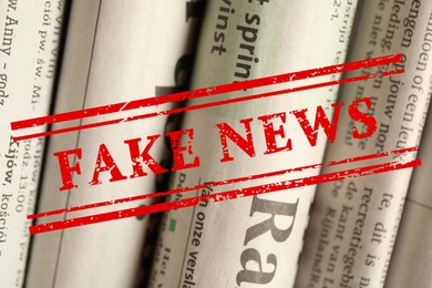 Image of Red Fake News stamp and newspapers in different languages as background, closeup