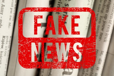 Image of Red Fake News stamp and newspapers in different languages as background, closeup
