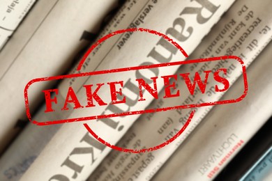 Image of Red Fake News stamp and newspapers in different languages as background, closeup