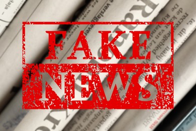 Image of Red Fake News stamp and newspapers in different languages as background, closeup