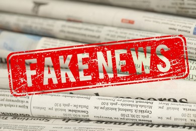 Image of Red Fake News stamp and newspapers as background, closeup