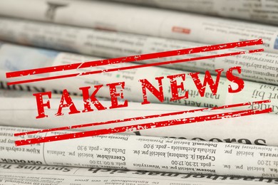 Image of Red Fake News stamp and newspapers as background, closeup