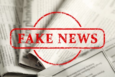 Image of Red Fake News stamp and newspapers as background, closeup