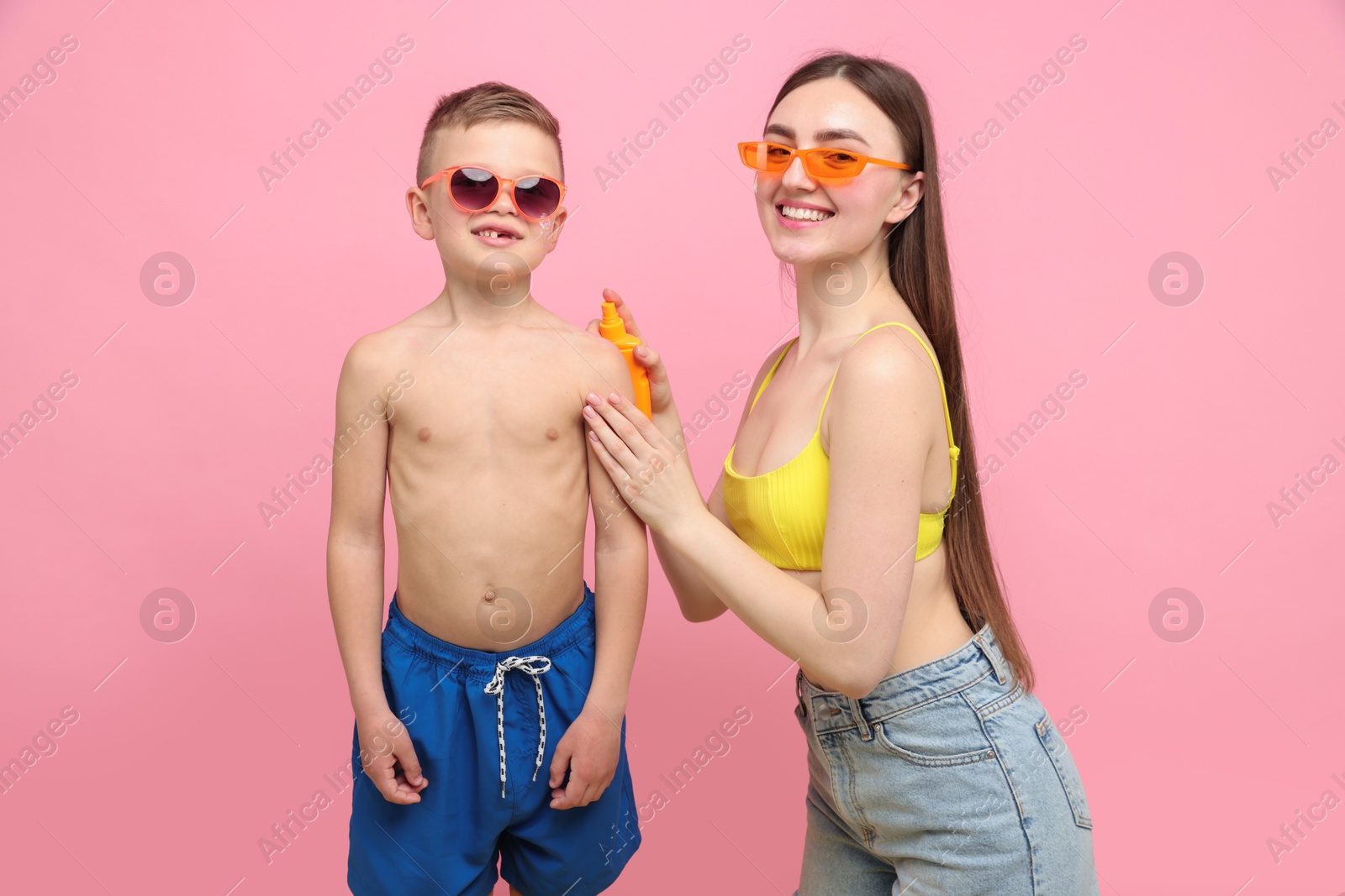 Mother applying sun protection cream onto her son's skin on pink background Photo of Mother applying sun protection cream onto her son's skin on pink background