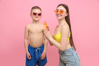 Photo of Mother applying sun protection cream onto her son's skin on pink background