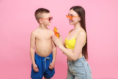 Photo of Mother applying sun protection cream onto her son's skin on pink background