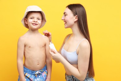 Photo of Mother applying sun protection cream onto her son's skin on yellow background