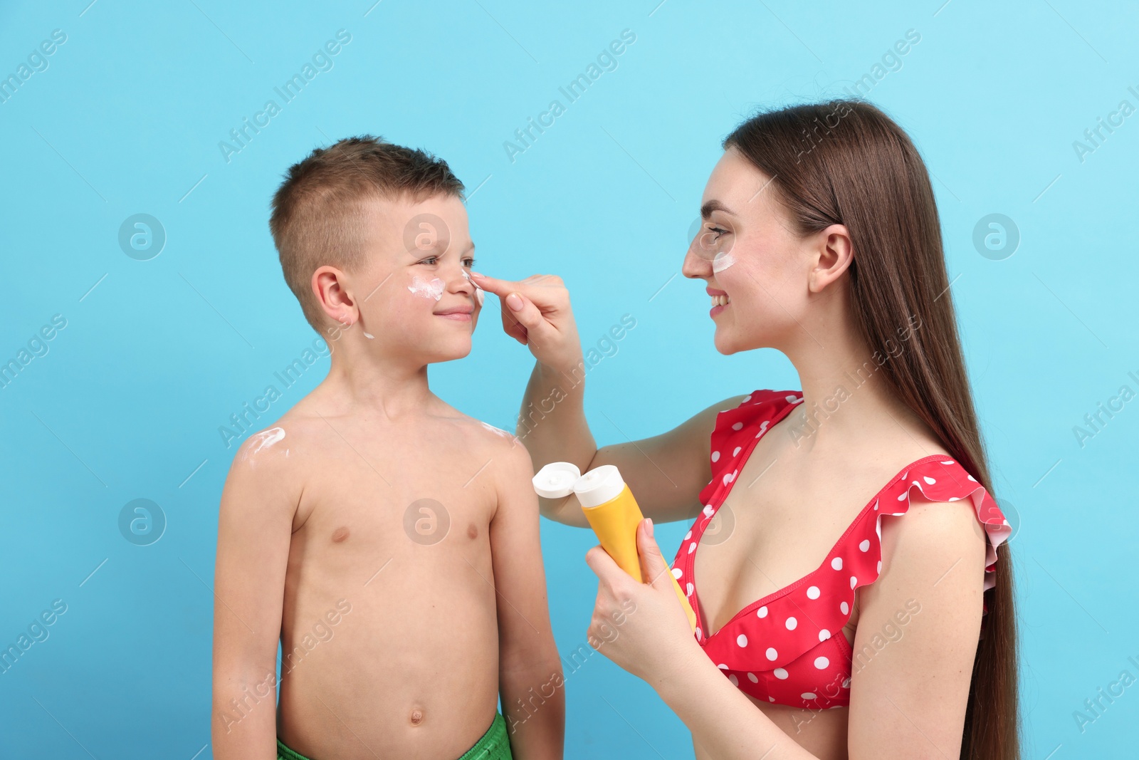 Mother applying sun protection cream onto her son's skin on light blue background Photo of Mother applying sun protection cream onto her son's skin on light blue background