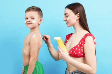 Photo of Mother applying sun protection cream onto her son's skin on light blue background