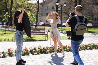 Photo of Professional photographers with reflector and camera near model during shooting outdoors on sunny day