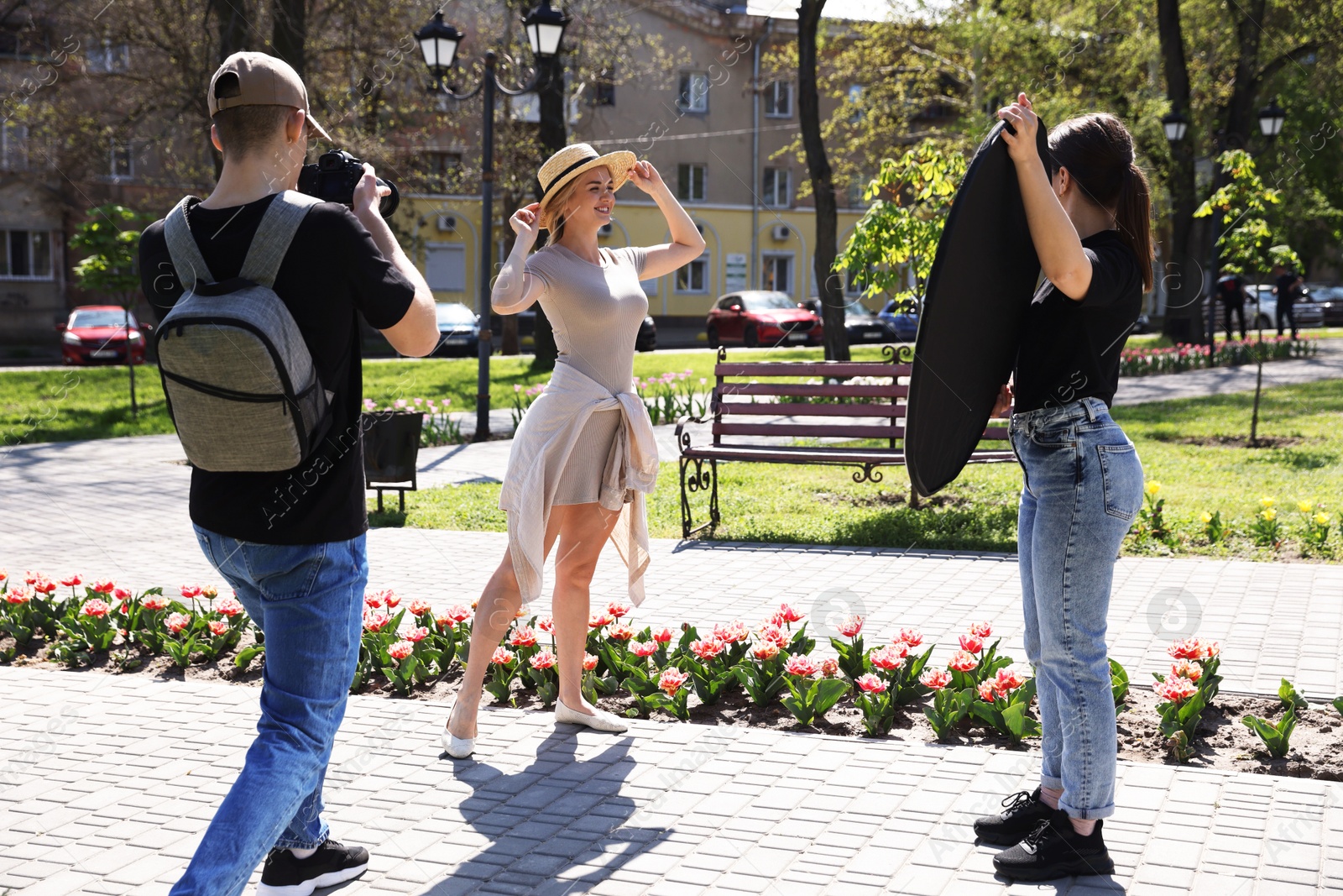 Professional photographers with reflector and camera near model during shooting outdoors on sunny day Photo of Professional photographers with reflector and camera near model during shooting outdoors on sunny day
