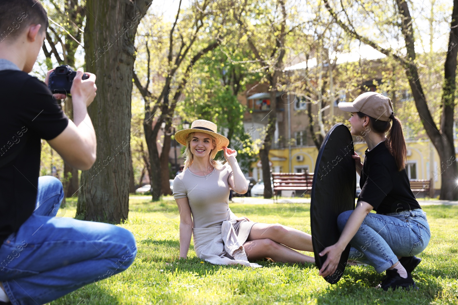 Professional photographers with reflector and camera near model during shooting outdoors on sunny day Photo of Professional photographers with reflector and camera near model during shooting outdoors on sunny day