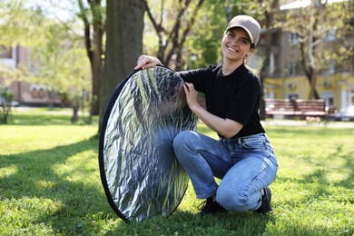 Photo of Woman with reflector outdoors on sunny day. Photography equipment