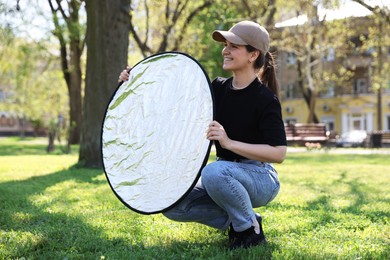 Photo of Woman with reflector outdoors on sunny day. Photography equipment