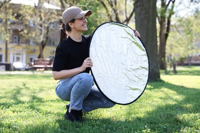 Photo of Woman with reflector outdoors on sunny day. Photography equipment