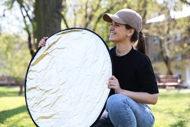 Photo of Woman with reflector outdoors on sunny day. Photography equipment