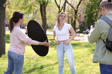 Photo of Professional photographers with reflector and camera near model during shooting outdoors on sunny day