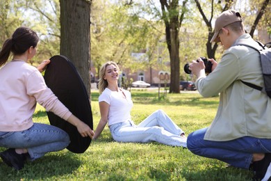 Photo of Professional photographers with reflector and camera near model during shooting outdoors on sunny day