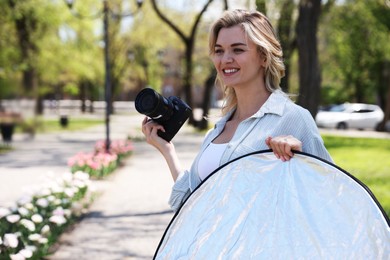 Photo of Professional photographer with reflector and camera outdoors on sunny day, space for text. Photography equipment