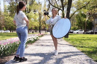 Photo of Professional photographer with reflector and camera near model during shooting outdoors on sunny day