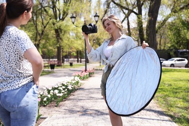 Photo of Professional photographer with reflector and camera near model during shooting outdoors on sunny day
