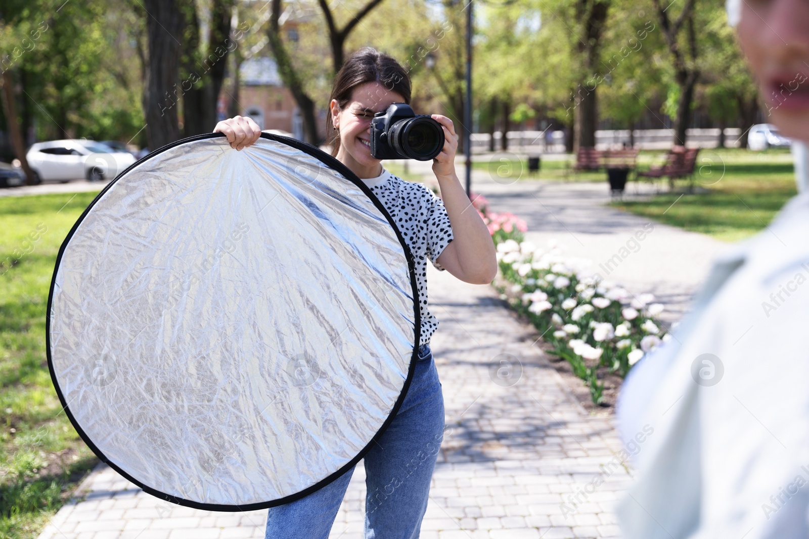 Professional photographer with reflector and camera near model during shooting outdoors on sunny day Photo of Professional photographer with reflector and camera near model during shooting outdoors on sunny day