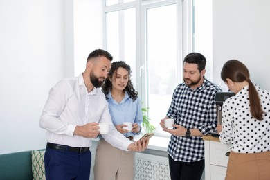 Photo of Man showing colleagues something on his phone during coffee break in office