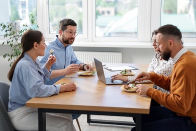 Photo of Colleagues eating and chatting during lunch break in office
