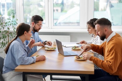 Photo of Colleagues eating and chatting during lunch break in office