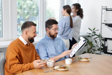 Photo of Colleagues eating and discussing work during lunch break in office