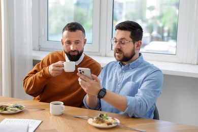 Photo of Man showing his colleague something on smartphone during lunch break in office