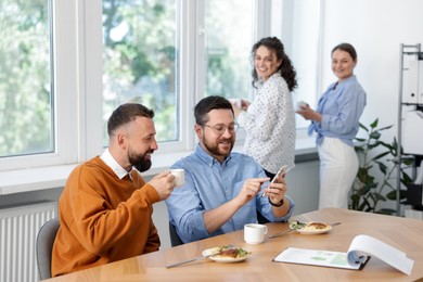 Photo of Man showing his colleagues something on smartphone during lunch break in office