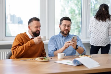 Photo of Man showing his colleagues something on smartphone during lunch break in office