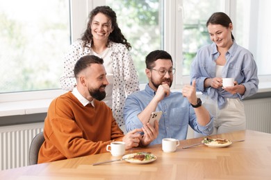 Photo of Man showing his colleagues something on smartphone during lunch break in office